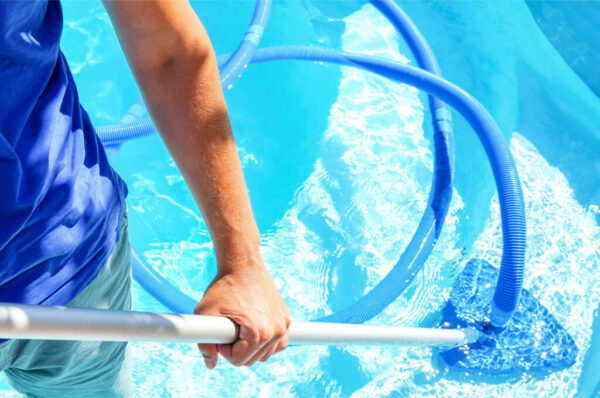 Service team member holding brush and hose while cleaning pool